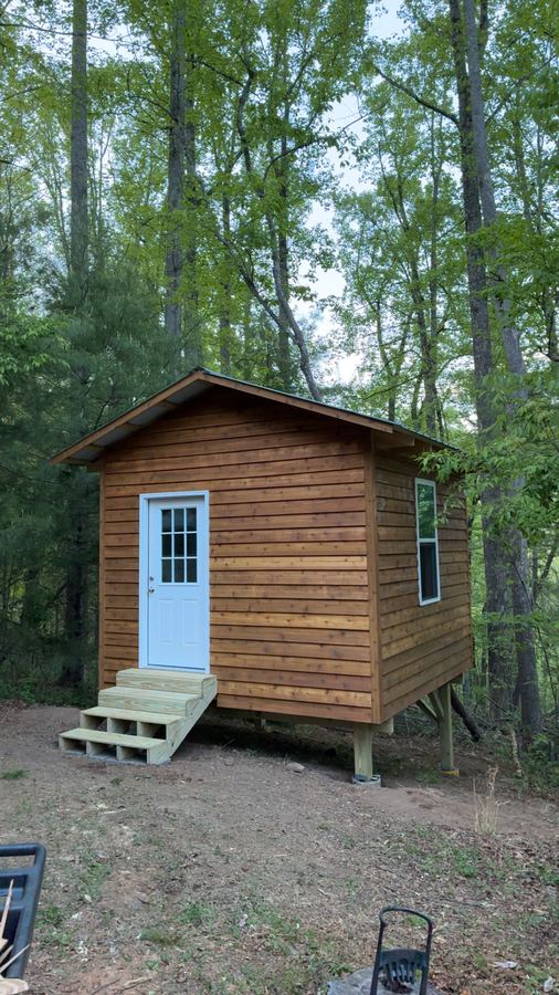 Cedar-sided storage shed on timber posts with a white door, a window and new steps